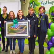 A group of women from Pets Foundation and Birmingham Dogs Home holding a framed picture of the new behavioural unit with green and purple balloons on each side of them.